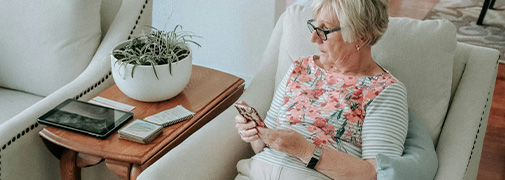 A senior-aged woman using a cell phone with a tablet nearby