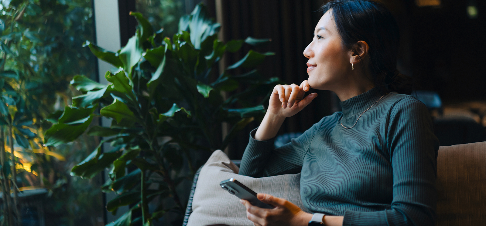 Asian woman looking out window with phone